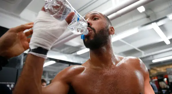 A boxer, hand-wrapped, drinks from a water bottle. This shows why boxers spit out water: to stay hydrated without swallowing too much.