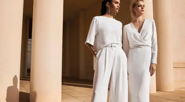 Due donne eleganti in bianco, un'ispirazione su come vestirsi ad un matrimonio con pantaloni ampi o abito longuette.