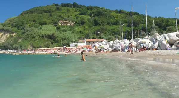 Spiaggia affollata a Gabicce Mare, con gente che nuota e prende il sole sotto un cielo azzurro.
