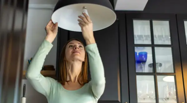 Mujer cambia bombilla en lámpara. ¿Se puede vender una casa sin luz ni agua? Quizás, pero con luz es más fácil.