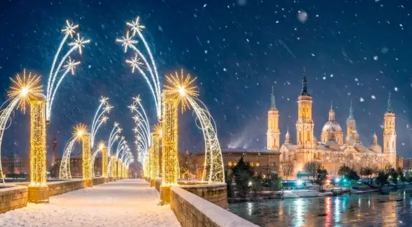 Puente nevado con encendido luces navidad Zaragoza. La Basílica del Pilar brilla bajo la nieve.