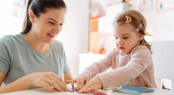 Bambina e maestra giocano con i puzzle in un asilo nido.