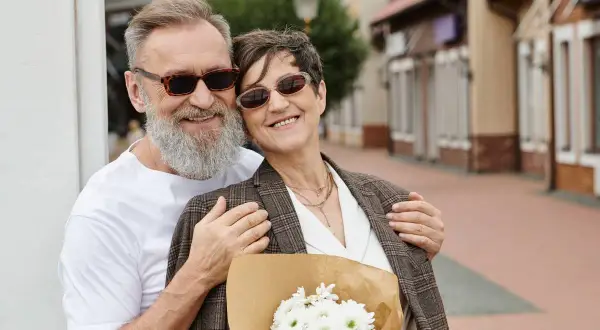 Szczęśliwa para świętuje rubinowe gody, trzymając bukiet kwiatów na tle ulicy z kamienicami.