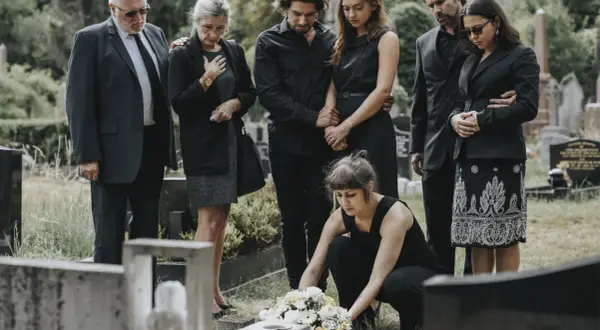Trauernde Familie in schwarzer Beerdigungskleidung legt Blumen nieder.