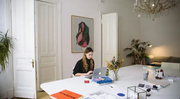 Młoda kobieta pracuje przy laptopie w jasnym pokoju. Czy Wielki Czwartek to święto? Zastanawia się, przeglądając notatki.