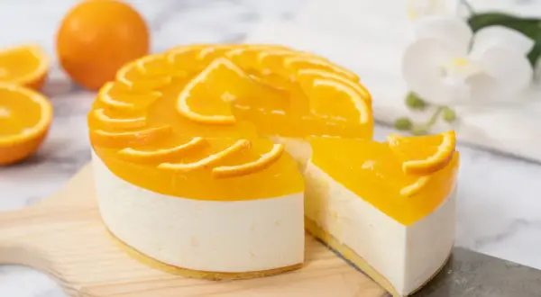 Sernik pomarańczowy z mascarpone, ozdobiony plasterkami pomarańczy, wygląda apetycznie. Kawałek ciasta został już odkrojony.