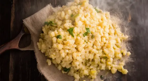 Gorąca kasza bulgur gotowanie na drewnianym stole, parująca i ozdobiona zielonymi ziołami.