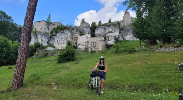 Kobieta z rowerem na tle ruin zamku na Szlaku Orlich Gniazd.