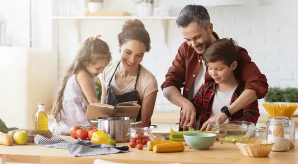 Famille préparant un repas. Le père aide son fils à couper des légumes. La mère et la fille consultent un livre de recettes. On se demande : lactose c'est quoi ?