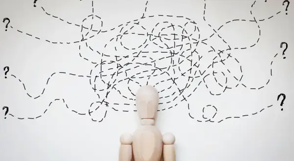 Drewniany manekin z chaotycznymi liniami i znakami zapytania nad głową, symbolizującymi trudności w diagnozie, np. borderline ICD 10.