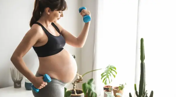 Mujer embarazada levanta mancuernas, cuidando su cuerpo. Evita ejercicios prohibidos embarazo primer trimestre.