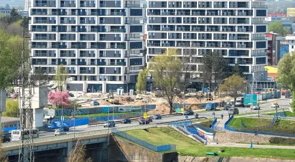 Nowe mieszkania do wynajęcia Rzeszów. Nowoczesne apartamentowce w budowie, ruchliwa droga i most.