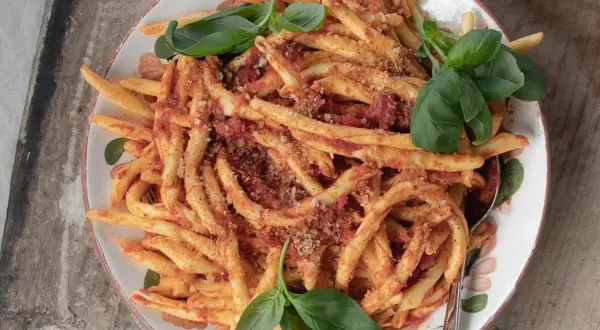 En skål med nduja pasta, toppad med färsk basilika och en citron i bakgrunden.
