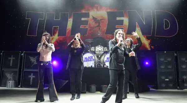Członkowie Black Sabbath na scenie podczas koncertu "The End". Ozzy Osbourne z mikrofonem, pozostali członkowie klaszczą.