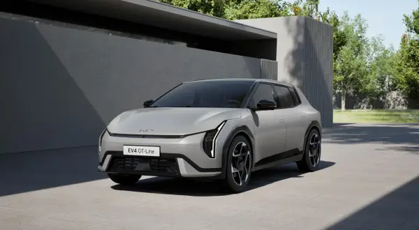 Nowy Kia EV4 GT-Line w kolorze srebrnym, zaparkowany przed nowoczesnym budynkiem z zielenią w tle.