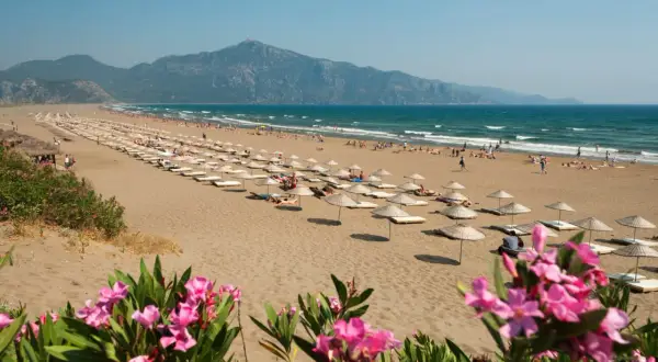 Piękna plaża w Turcji, gdzie turcja w marcu pogoda sprzyja relaksowi pod parasolami. W tle góry i turkusowe morze.