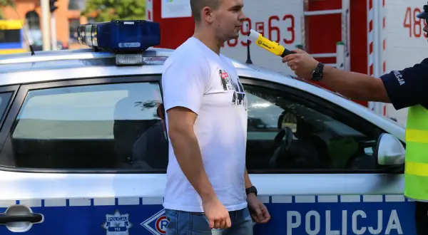 Policjant bada alkomatem mężczyznę obok radiowozu.