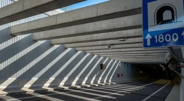 Droga wjazdowa do tunelu z betonowymi belkami i znakiem informującym o długości 1800m.