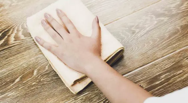 Mano che pulisce un pavimento in legno con un panno, per rimuovere lo sporco e far brillare il legno annerito.