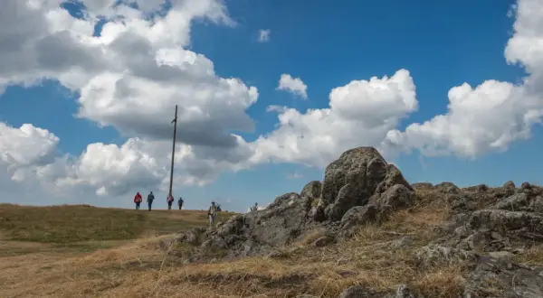 Wanderer auf dem Herzogenhorn genießen die Aussicht unter dramatischen Wolken. Ein Holzkreuz markiert den Gipfel.