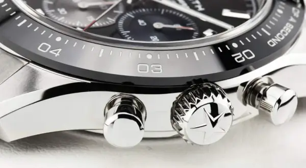 Detalle de un reloj de lujo, mostrando el bisel con números y marcas, y los pulsadores. El bisel del reloj está diseñado para cambiar la hora.