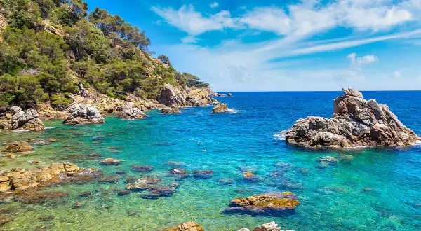 Piękna pogoda w Lloret de Mar w czerwcu. Turkusowa woda, skaliste wybrzeże porośnięte zielenią, błękitne niebo z chmurkami.