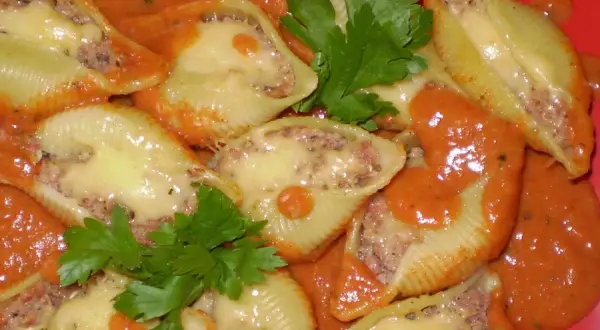 Nadziewane muszle makaronowe mięsem mielonym, zapieczone z serem i polane sosem pomidorowym.
