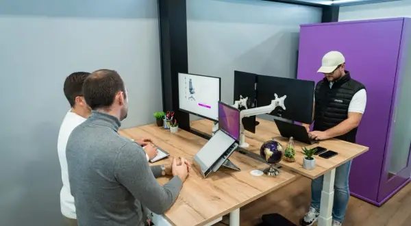 Trois personnes travaillent dans un bureau flex office moderne. L'un est debout devant un écran, les deux autres sont assis à un bureau.