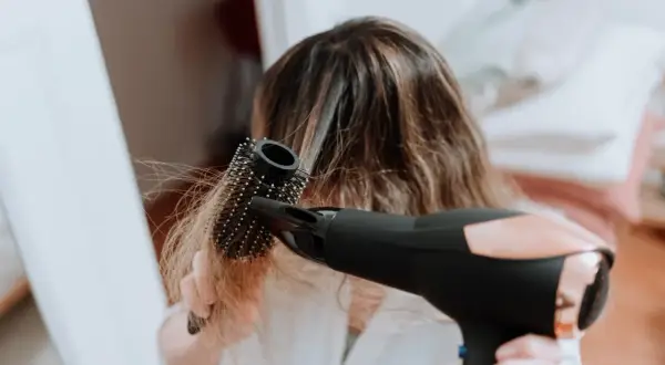 Frau föhnt ihre Haare mit einer Rundbürste, um fliegende Haare zu bändigen.