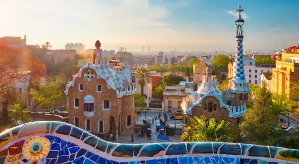 Kolorowa mozaika Parku Güell wita na wspaniałej **barcelona wycieczka**. Dwa bajkowe domki i wieża z krzyżem w tle.