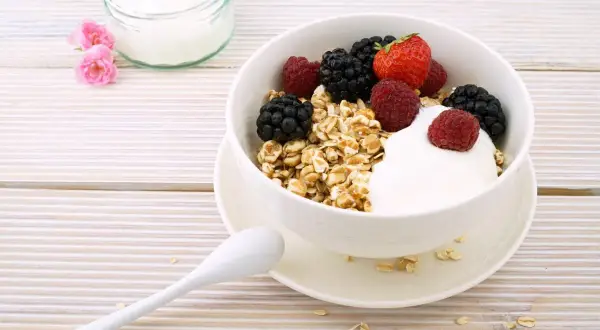 Un delizioso yogurt a colazione con muesli e frutti di bosco freschi, pronto per iniziare la giornata con energia e gusto.