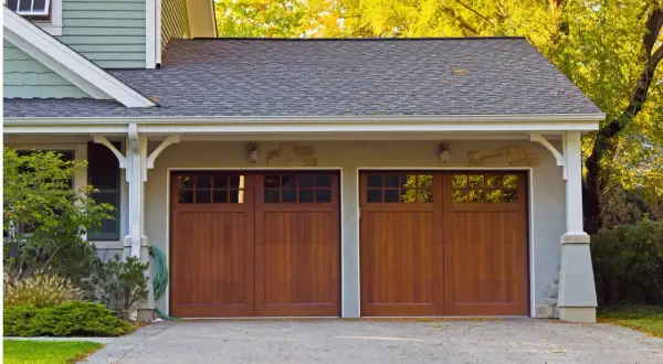 Doppio garage con porte in legno scuro, un box di pertinenza si può vendere separatamente. Alberi autunnali sullo sfondo.