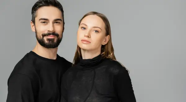 Para, która uosabia styl unisex. Mężczyzna z zarostem i kobieta o delikatnych rysach, oboje w czarnych, prostych ubraniach.
