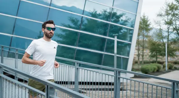 Uomo con occhiali da sole corre su una rampa metallica, godendosi i suoi 30 secondi di recupero tra le serie di allenamento.