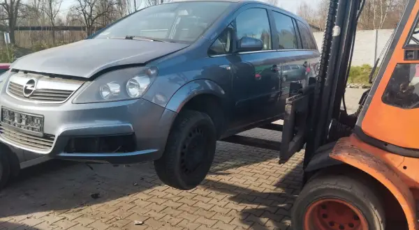 Szary Opel Zafira na złomowisku, podnoszony przez wózek widłowy. Dowiedz się, ile kosztuje złomowanie auta.