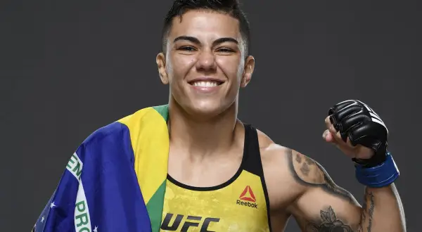 Jessica Andrade, MMA-fighter, ler glatt med Brasiliens flagga över axeln och en boxningshandske på sin högra hand.