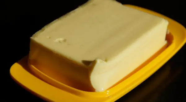 Kostka masła w żółtym naczyniu, gotowa do smarowania. Zastanawiasz się, ile ma kostka masła?