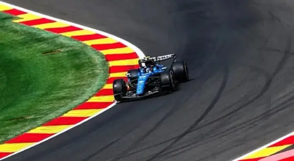 Un coche azul de Fórmula 1 toma una curva cerrada en la pista, con la hierba y las rayas rojas y amarillas de la escapatoria a su lado. La clasificación de Fórmula 1 hoy promete emoción.