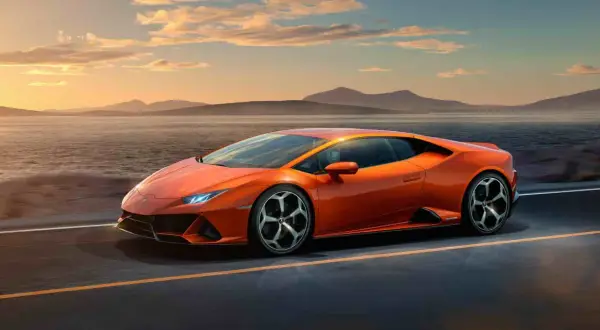 Pomarańczowy Lamborghini Huracan Evo pędzi wzdłuż malowniczego wybrzeża o zachodzie słońca.
