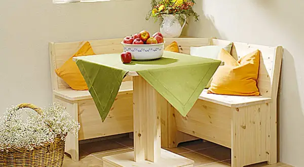 Holzige Eckbank mit Schlaffunktion selber bauen: Gemütliche Sitzecke mit Tisch, Äpfeln und Blumenkorb.