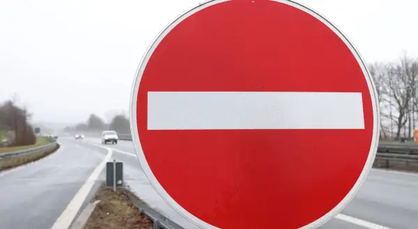 Ein rotes Rundschild mit weißem Balken: durchfahrt verboten schild. Autos fahren auf nasser Straße im Hintergrund.