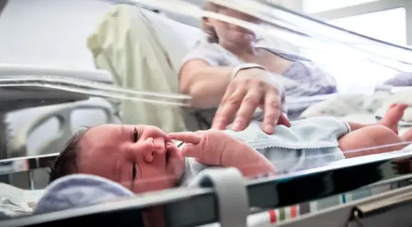 Noworodek, dziecko urodzone w 36 tygodniu, leży w inkubatorze. Mama delikatnie dotyka jego paluszka.