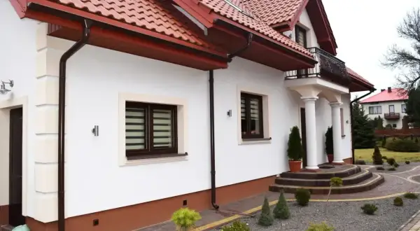 Elegancki cokół budynku z brązowym wykończeniem, ozdobiony kamieniami i miniaturowymi drzewkami.