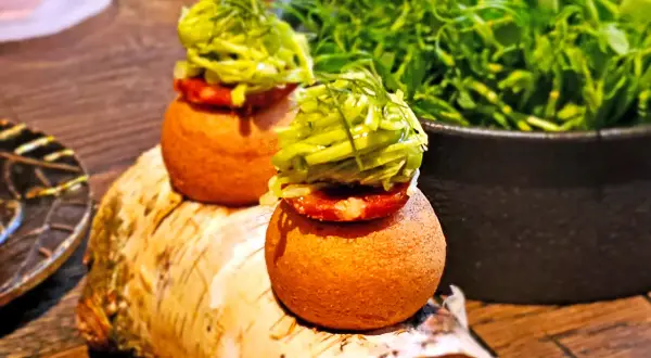 Dwa apetyczne mini-burgerki z zielonymi dodatkami, serwowane na pniu brzozy. Idealne na przekąskę, jak w najlepszych **bottiglieria 1881 opinie**.