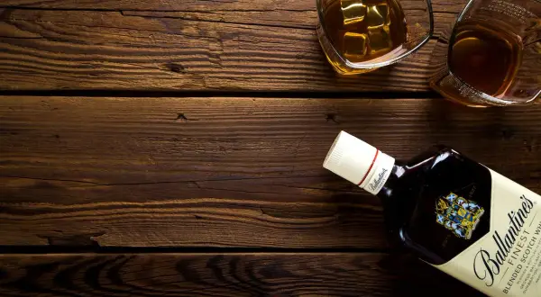 Butelka Ballantine's i dwa kieliszki z whisky na drewnianym stole. Pamiętaj o chorwacja limity alkoholu podczas podróży.