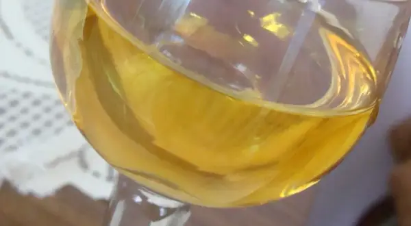Złocisty płyn w kieliszku, być może aromatyczne wino mandarynkowe, odbija światło.