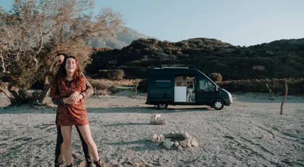 Glückliches Paar mit Hund im Campervan, genießt eine Kreta Rundreise auf eigene Faust am Strand.