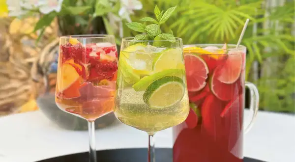 Tre glas med alkoholfri sangria fyllda med frukt och is. En kanna med röd sangria i bakgrunden.