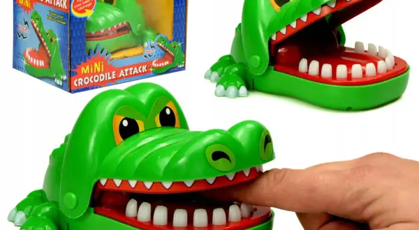 Zielona zabawka gra krokodyl z otwartą paszczą, do której włożono palec. Obok pudełko z napisem "Mini Crocodile Attack".