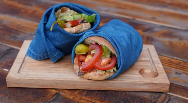 Två kebab i ugn, inslagna i jeans, serveras på en träbricka.